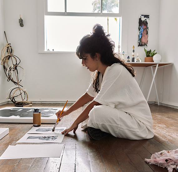 Female artist sitting on floor painting paper with black paint