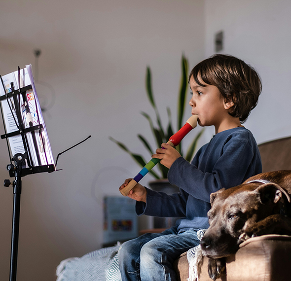Young boy sitting on couch playing a recorder in front of a music stand