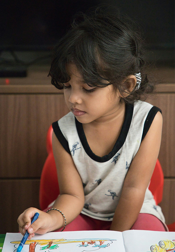 Young girl in white and black tank top, sitting in red chair coloring in coloring book